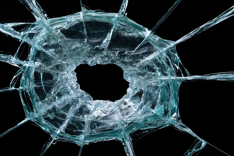 Shattered glass pane with central impact hole and radiating cracks against black background