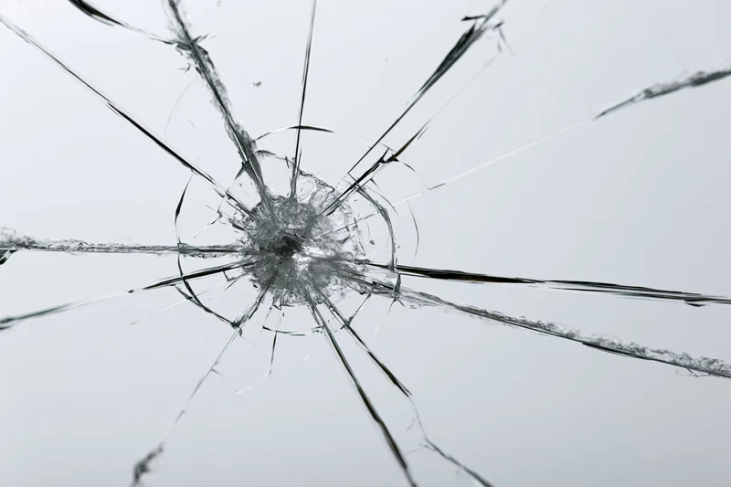 Shattered glass pane with radial cracks from central impact point