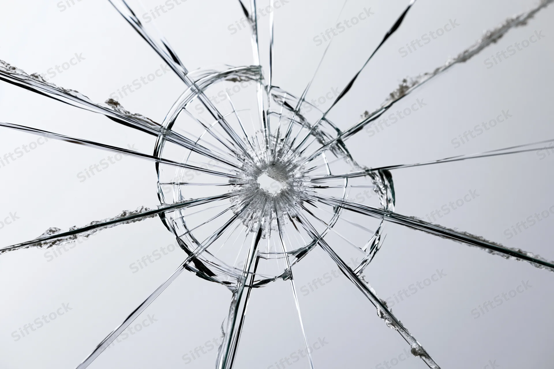 Shattered glass pane with radial cracks from central impact point against plain background