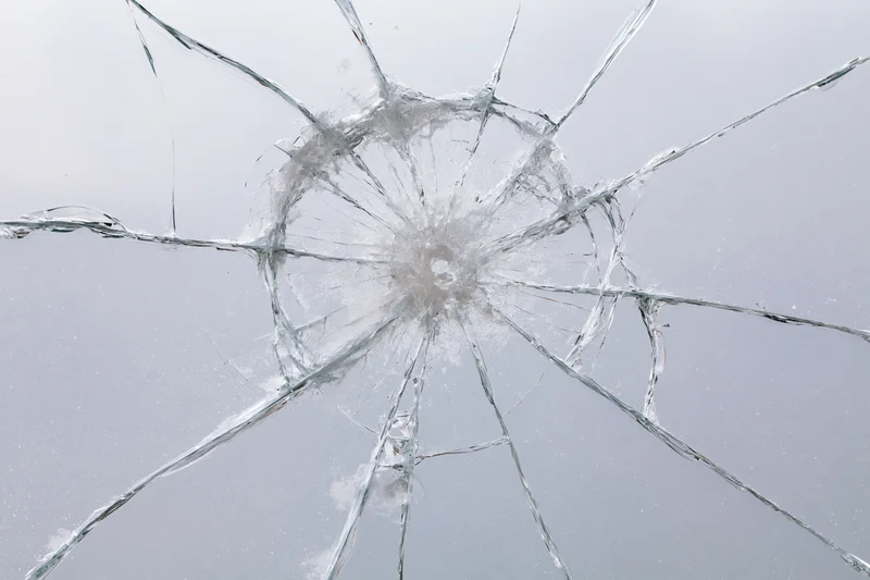 Shattered glass pane with radial cracks from central impact point