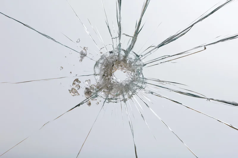 Shattered glass pane with central impact point radiating cracks across transparent surface