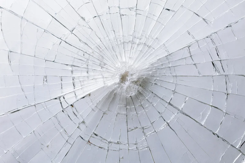 Shattered glass pane with radial cracks emanating from central impact point