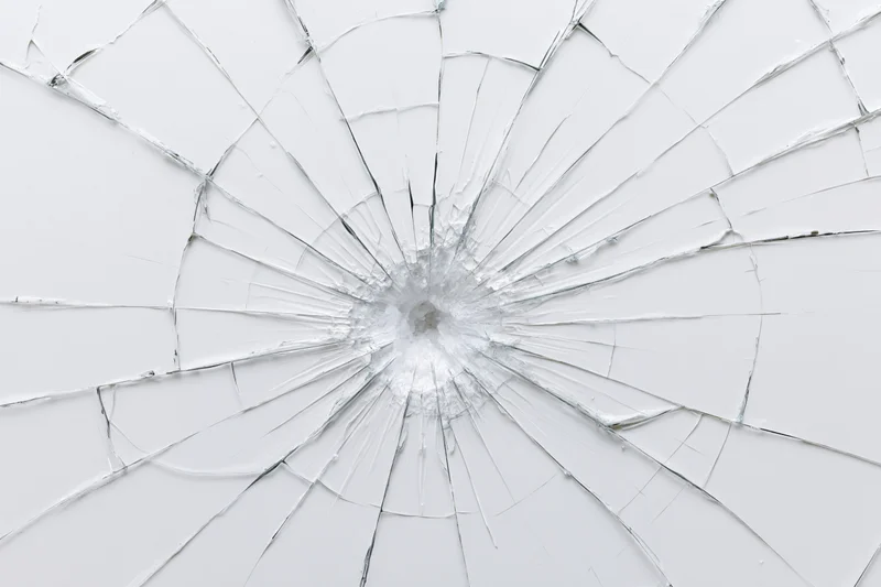 Shattered glass pane with radial cracks from central impact point against white background