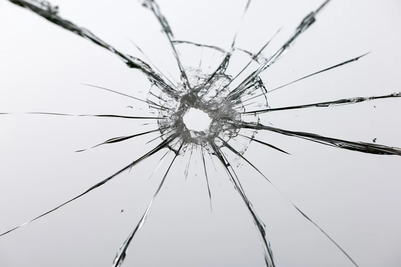 Shattered glass pane with central impact point radiating cracks across transparent surface