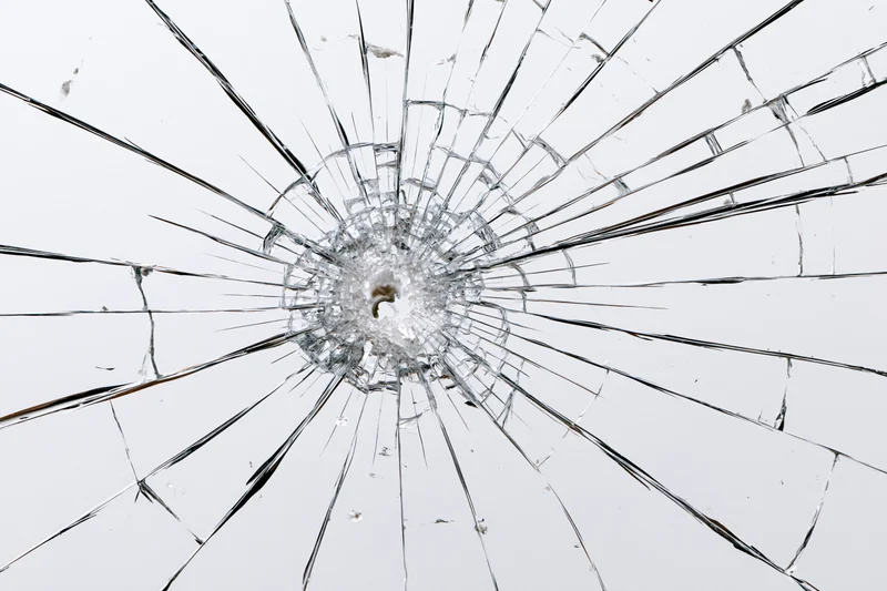 Shattered glass pane with central impact point radiating cracks across surface
