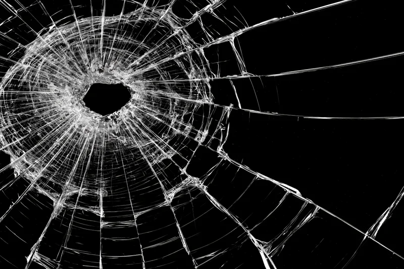 Shattered glass pane with central hole and radial cracks against black background