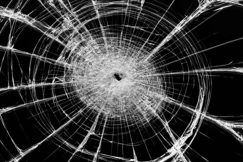 Shattered glass pane with radial cracks from central impact point against black background
