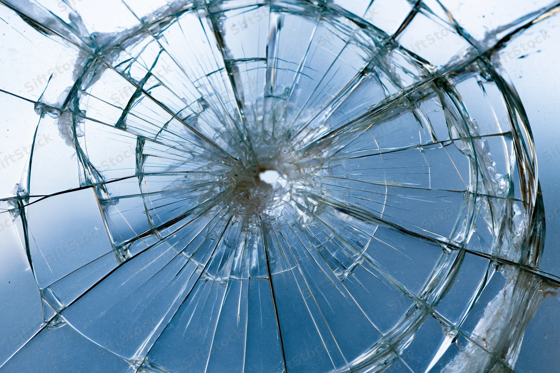 Shattered glass pane with radial cracks emanating from central impact point against blue background