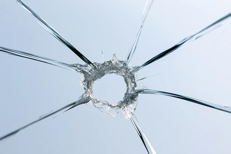 Shattered glass pane with jagged central hole and radiating cracks against light blue background