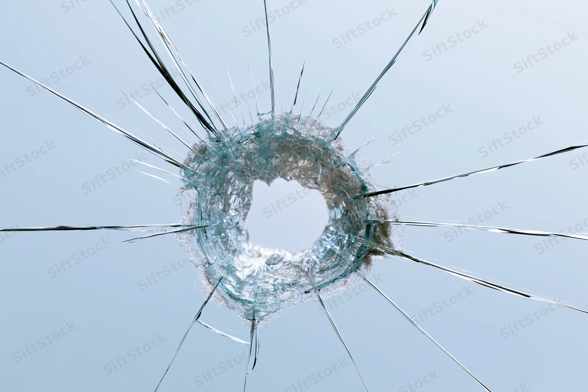 Shattered glass pane with a jagged central impact hole and radial cracks against a light blue background