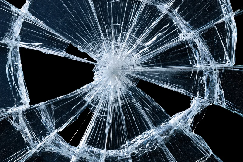 Shattered glass with radial cracks from central impact point against dark background