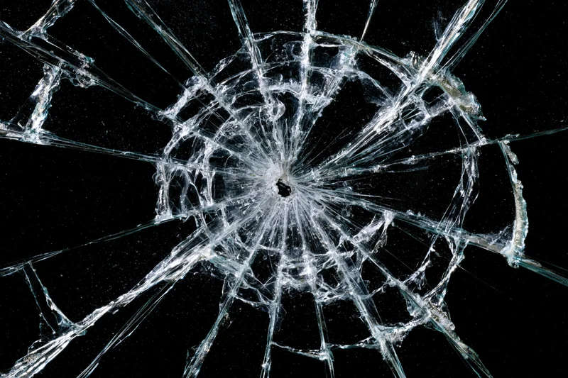 Shattered glass with a central impact point radiating cracks against a black background