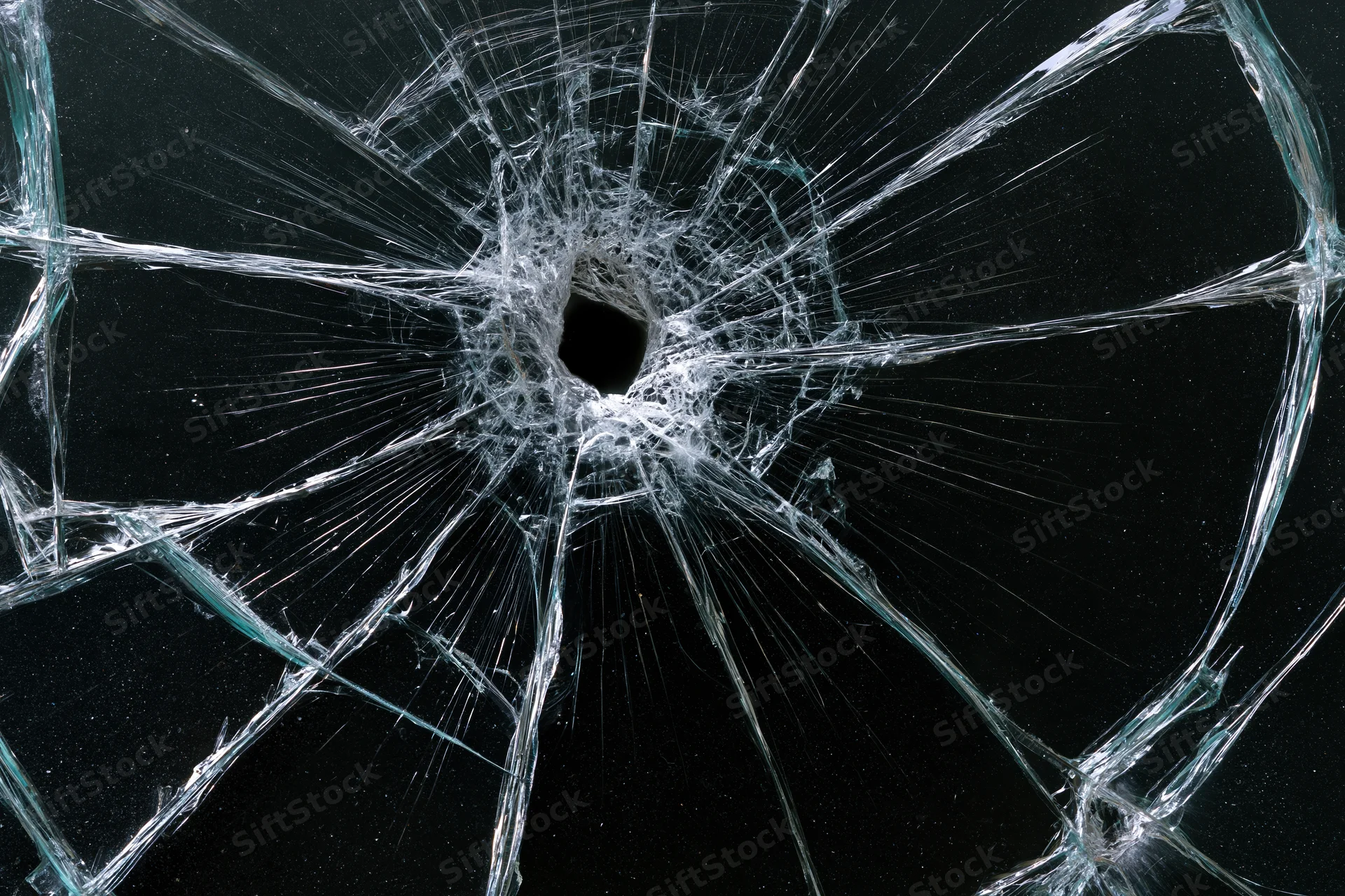 Shattered glass with a central hole and radiating cracks against a dark background