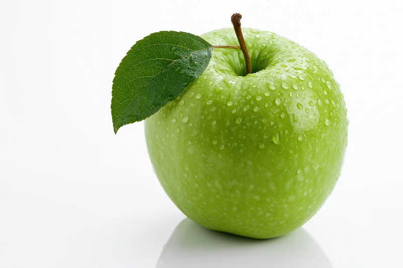 Single green Granny Smith apple with attached leaf and water droplets on white background