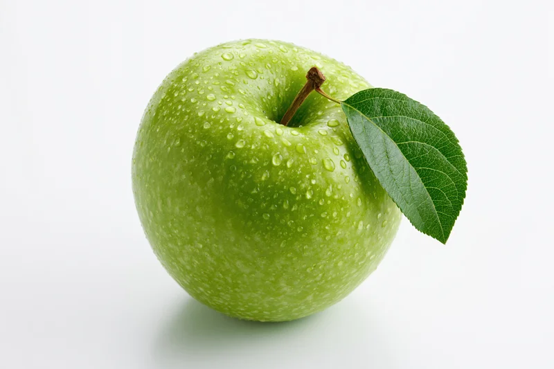 Single green apple with water droplets and attached leaf on white background