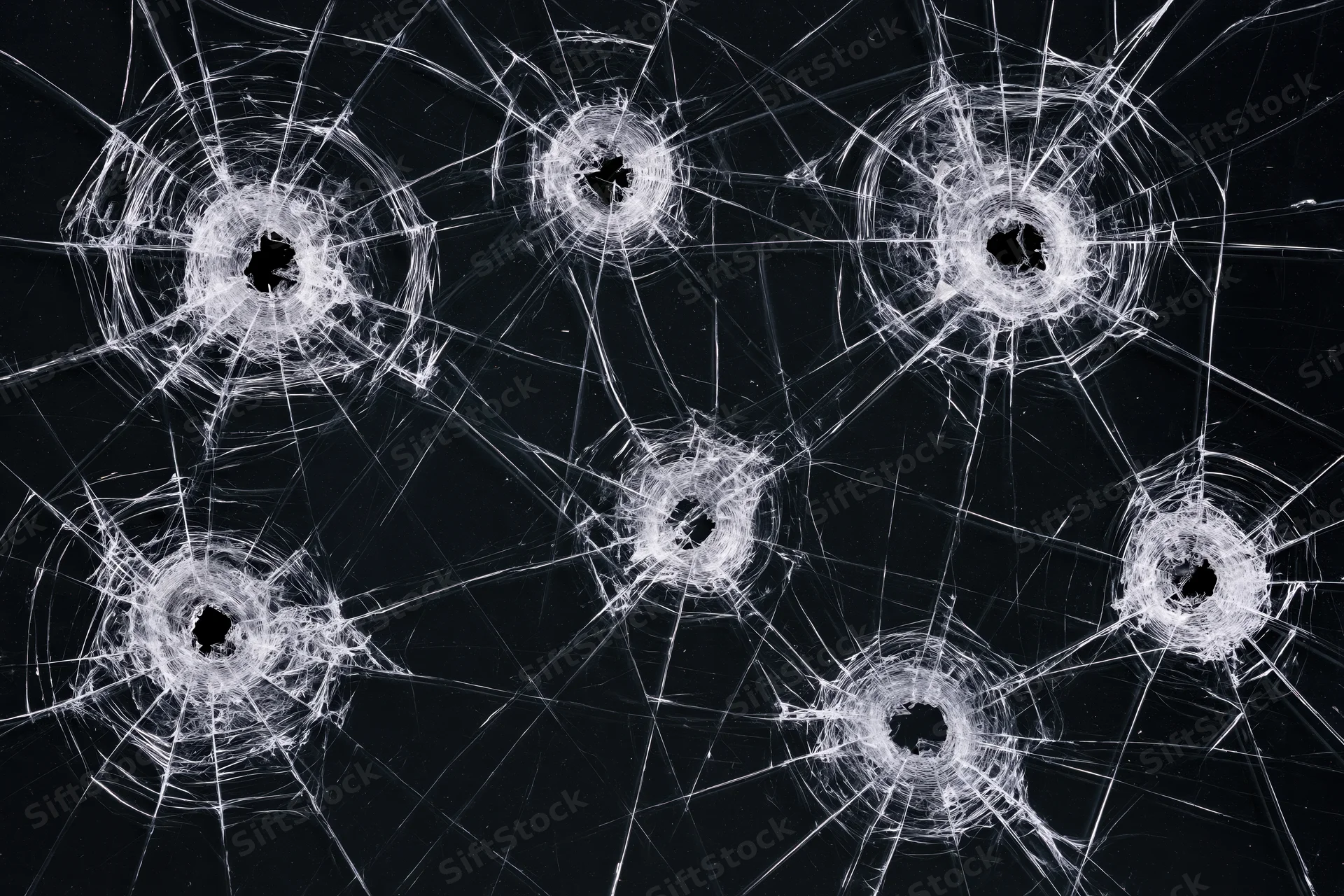 Six bullet holes in a dark tempered glass pane each with radial cracks spreading outward