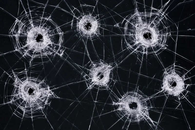 Six bullet holes in a dark tempered glass pane each with radial cracks spreading outward