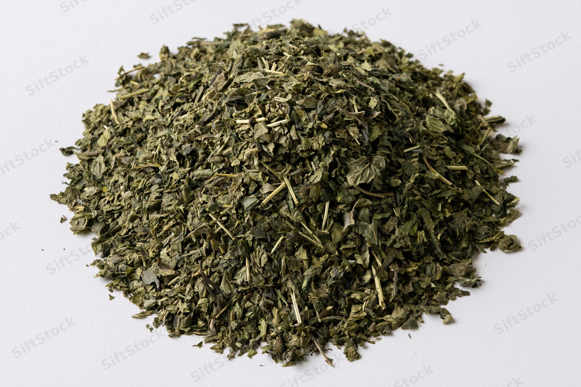 Loose pile of dried green herb leaves and stems overhead on white background