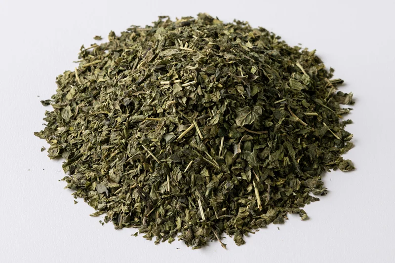 Loose pile of dried green herb leaves and stems overhead on white background