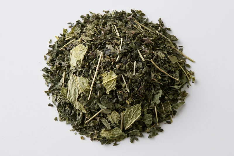 Loose pile of dried green herb leaves and stems on white background