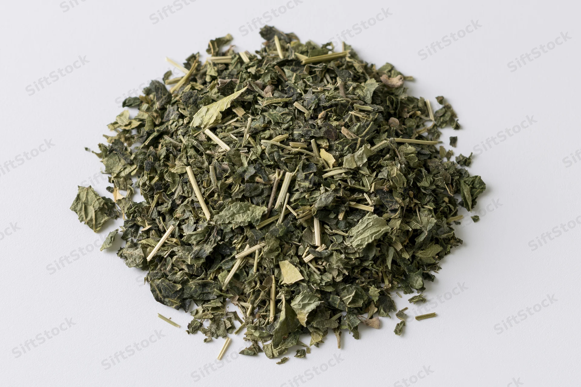 Loose pile of dried green herb leaves and stems on white background