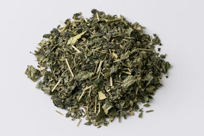 Loose pile of dried green herb leaves and stems on white background