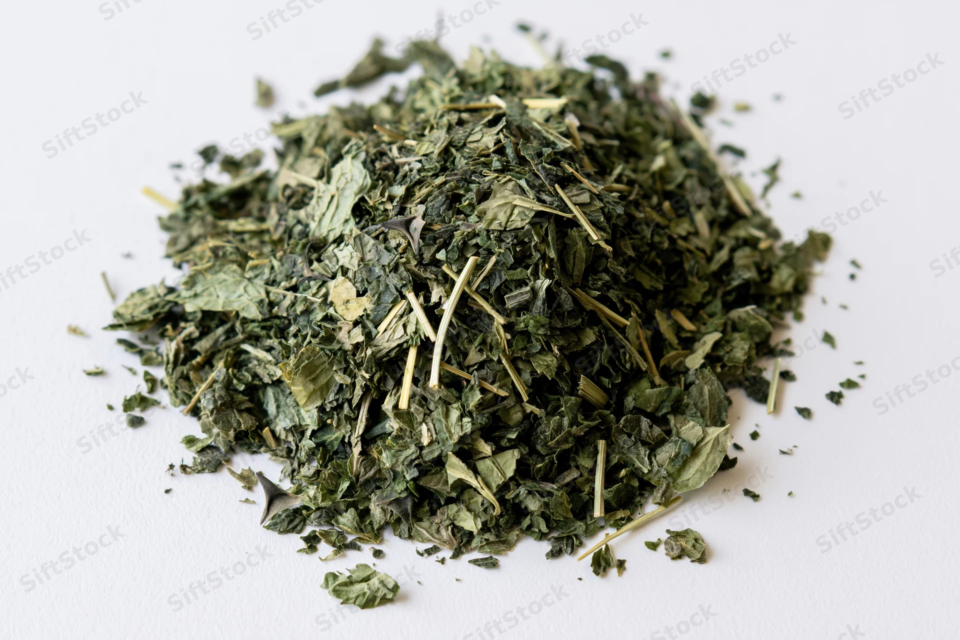 Loose pile of dried green herb leaves and stems on white surface