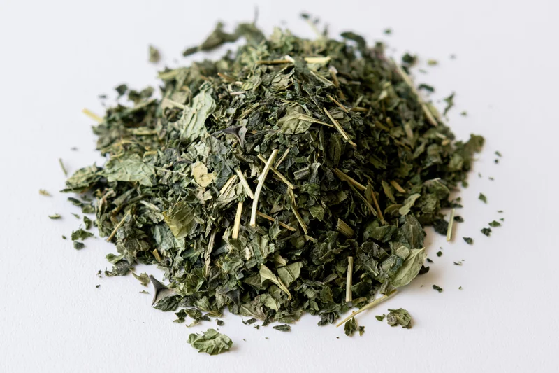 Loose pile of dried green herb leaves and stems on white surface