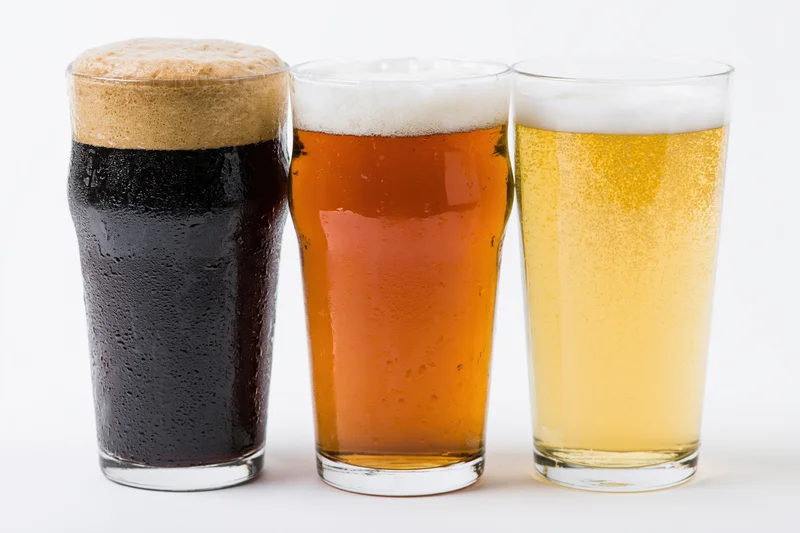 Three pint glasses of beer lined up side by side on a white background