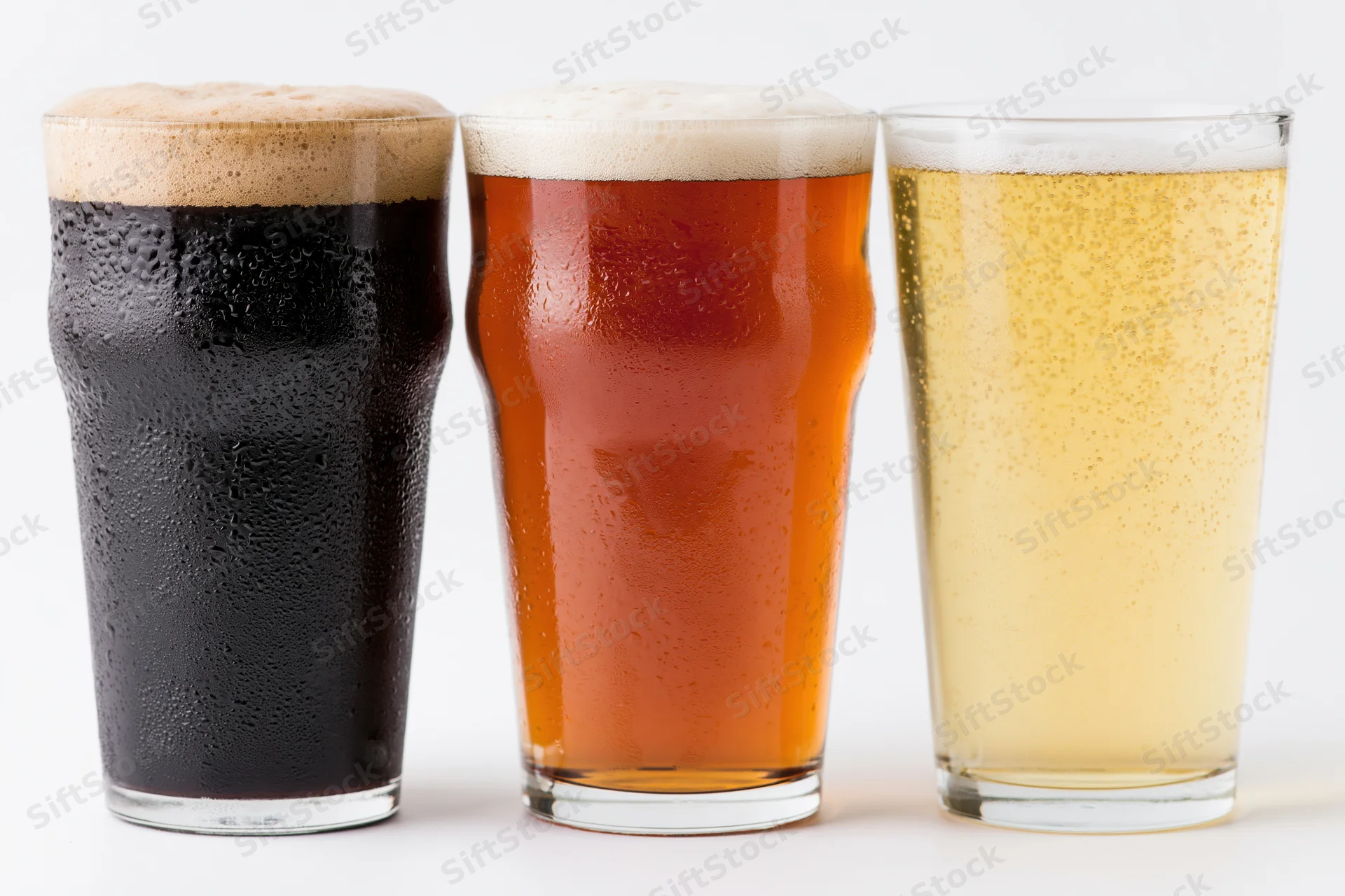 Three pint glasses of beer lined up side by side on a white surface