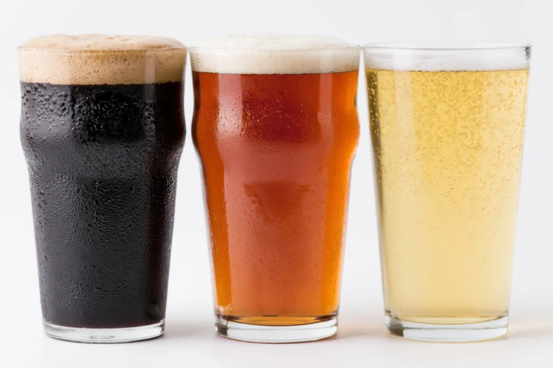 Three pint glasses of beer lined up side by side on a white surface