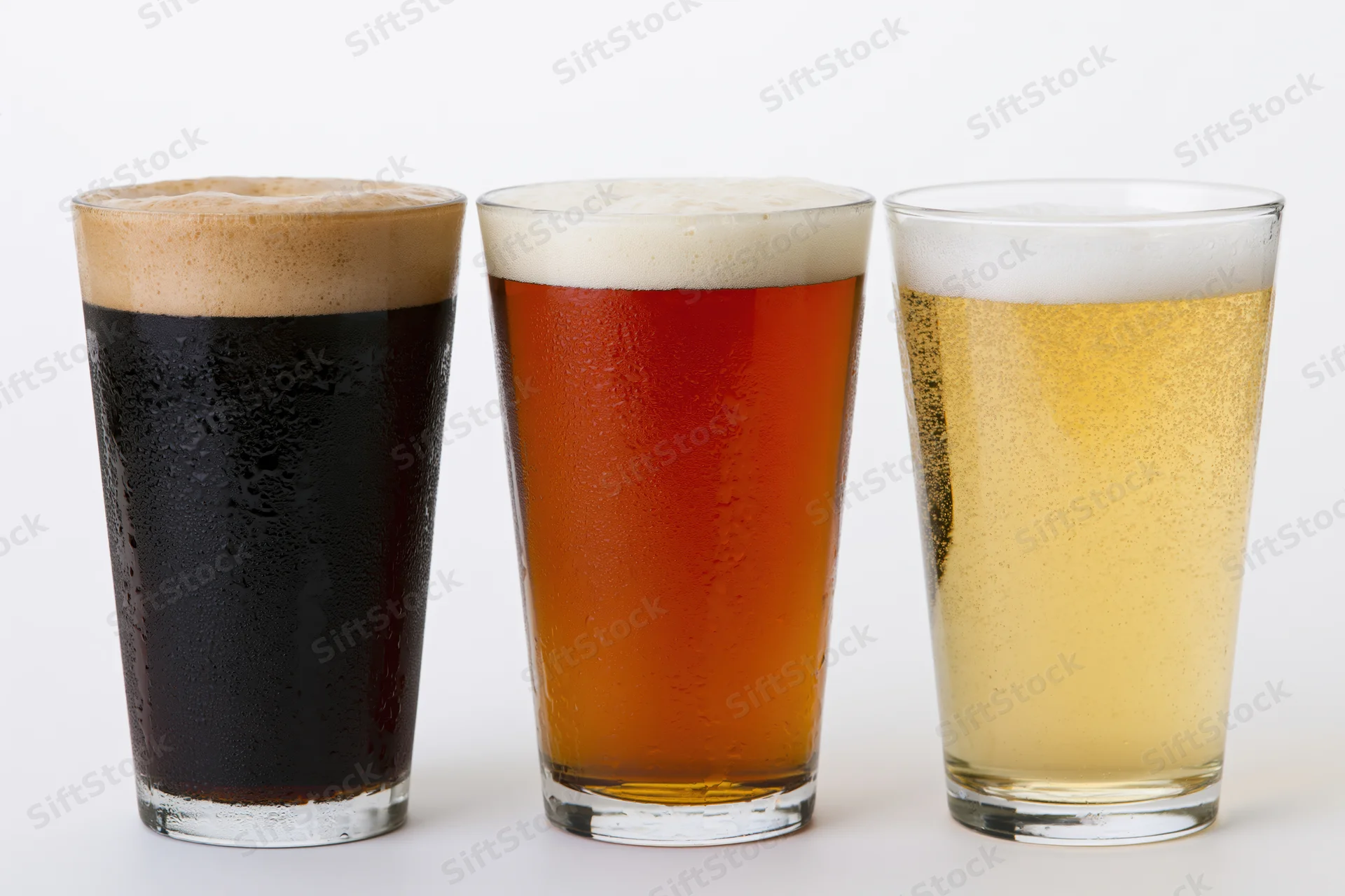 Three pint glasses of beer lined up side by side on a white background