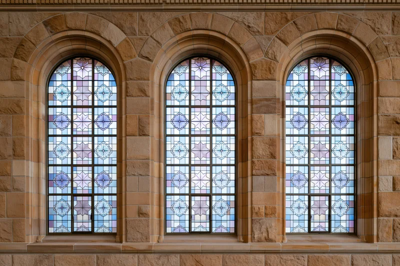 Three tall arched stained glass windows side by side on a stone building facade