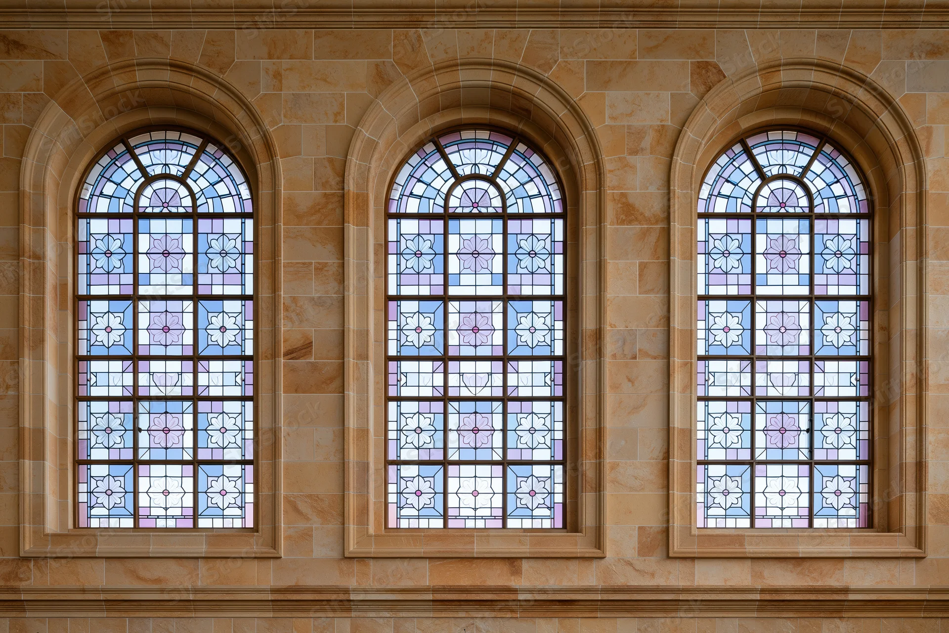 Three tall arched stained glass windows side by side on a stone building facade