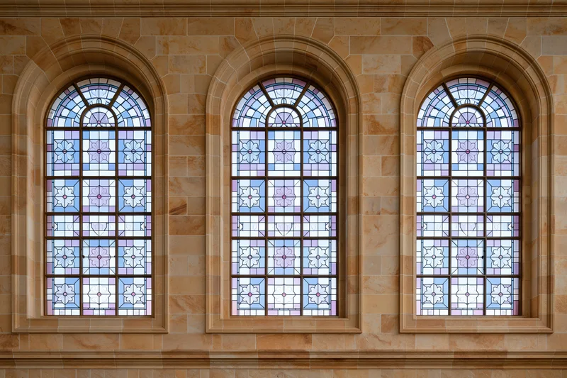 Three tall arched stained glass windows side by side on a stone building facade