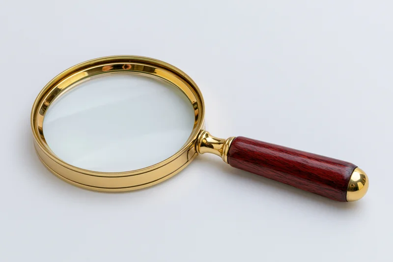 Vintage magnifying glass with polished brass frame and dark wooden handle on white background
