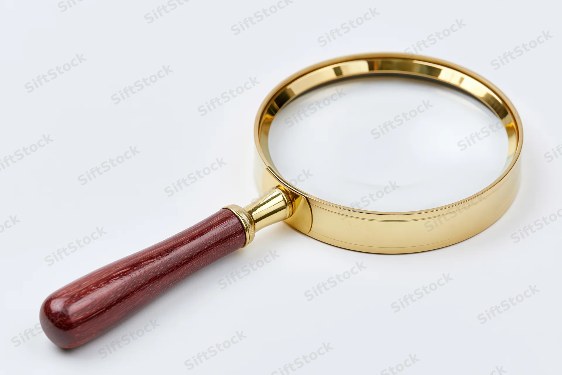 Vintage magnifying glass with polished brass frame and dark wooden handle on white background