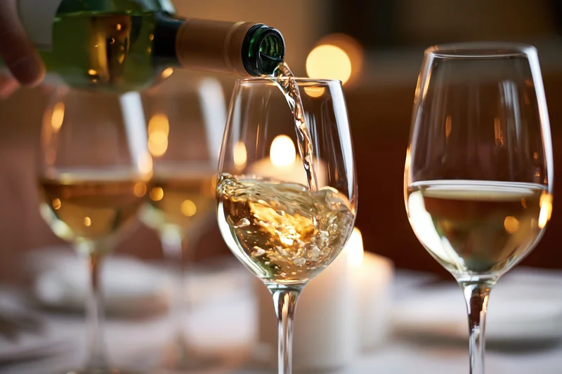 White wine being poured from a green bottle into a crystal glass at a candlelit dinner table