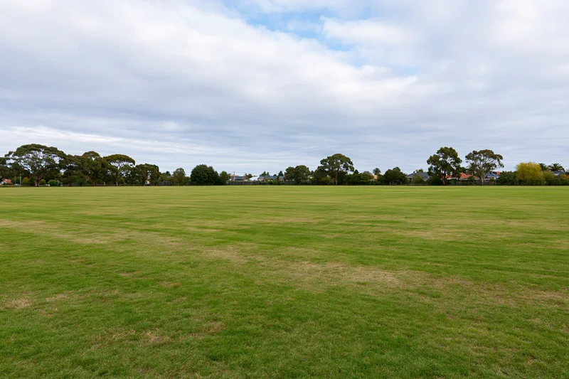 Wide open mown grass field stretching to a tree-lined suburban horizon under a cloudy sky