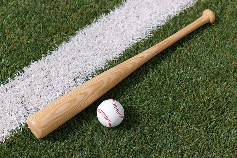 Wooden baseball bat and white leather baseball resting on grass field near white chalk line