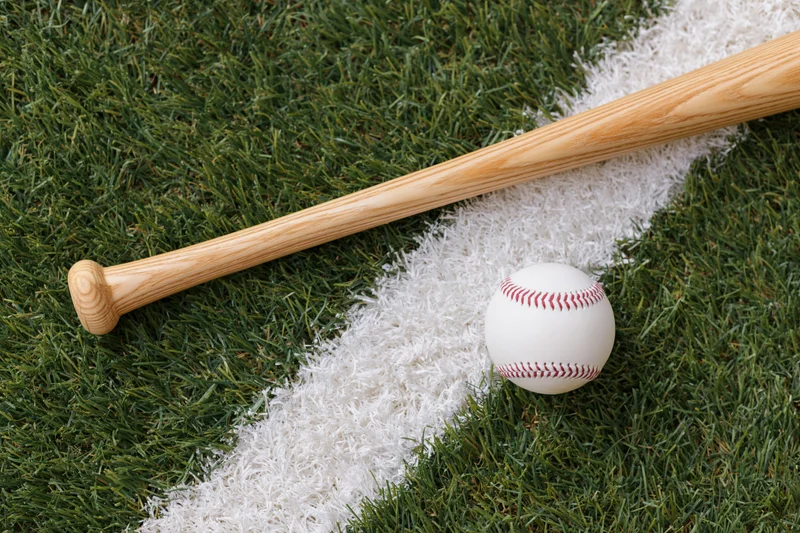 Wooden baseball bat and white leather baseball resting on grass field with chalk line