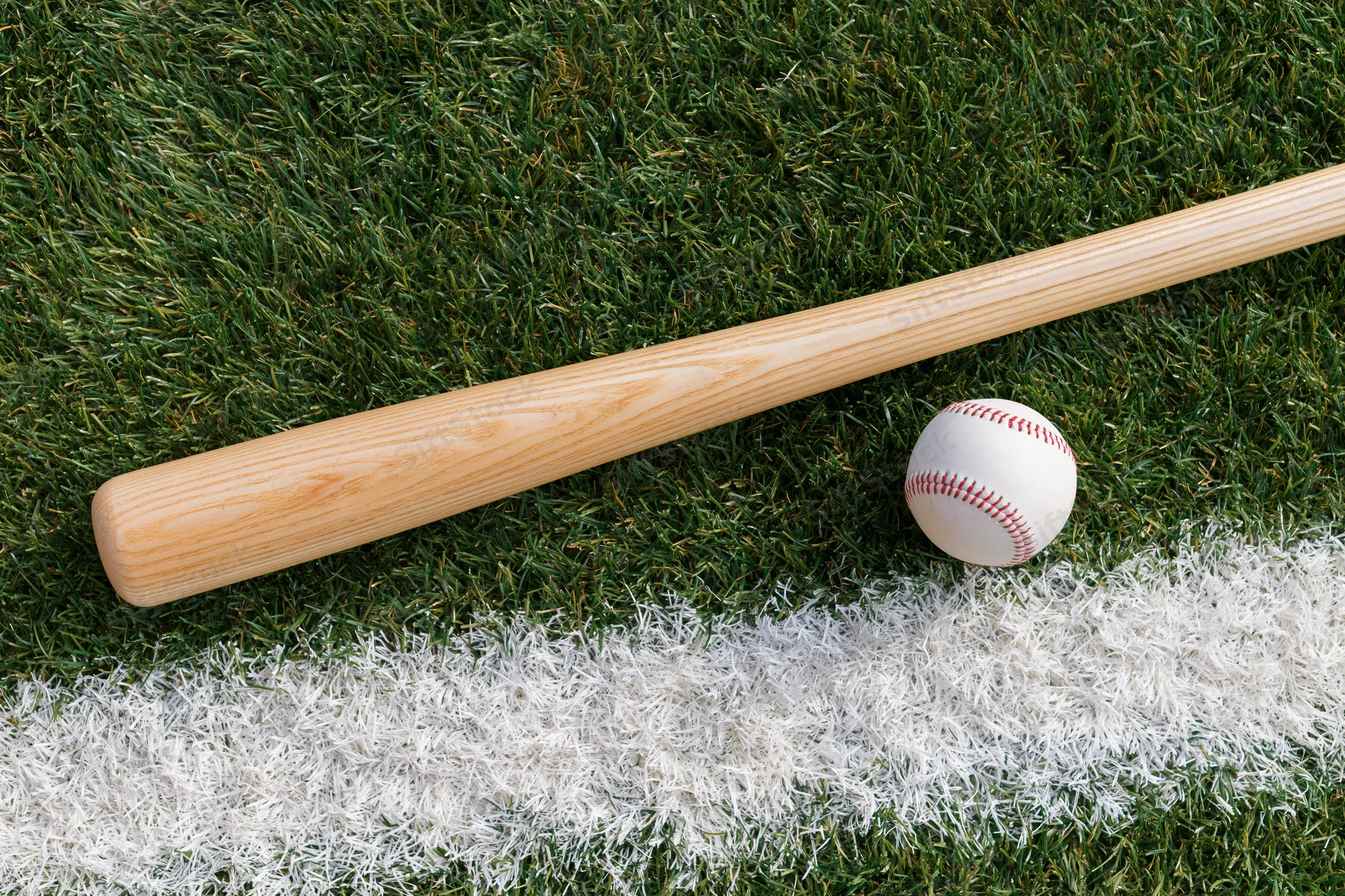 Wooden baseball bat and white leather baseball resting on grass field near white chalk line