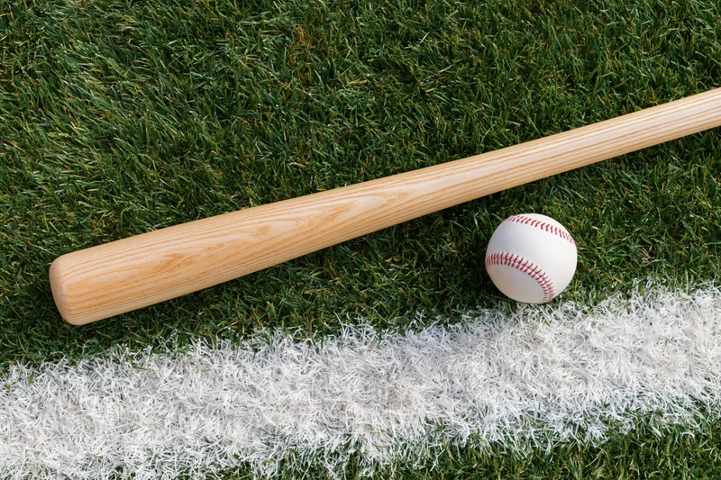 Wooden baseball bat and white leather baseball resting on grass field near white chalk line