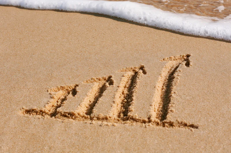 Roman numeral xiii written in sand near ocean wave