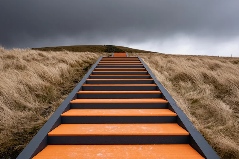 Bold geometric staircase with orange treads ascending a grassy hill under cloudy sky