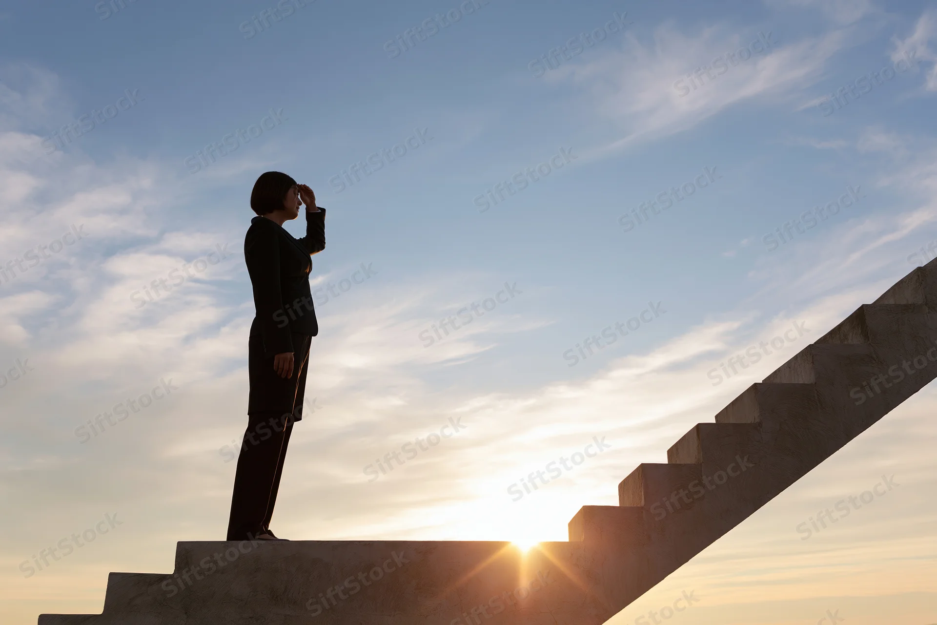 Businesswoman in silhouette standing on concrete staircase at sunrise, hand shielding eyes, looking upward