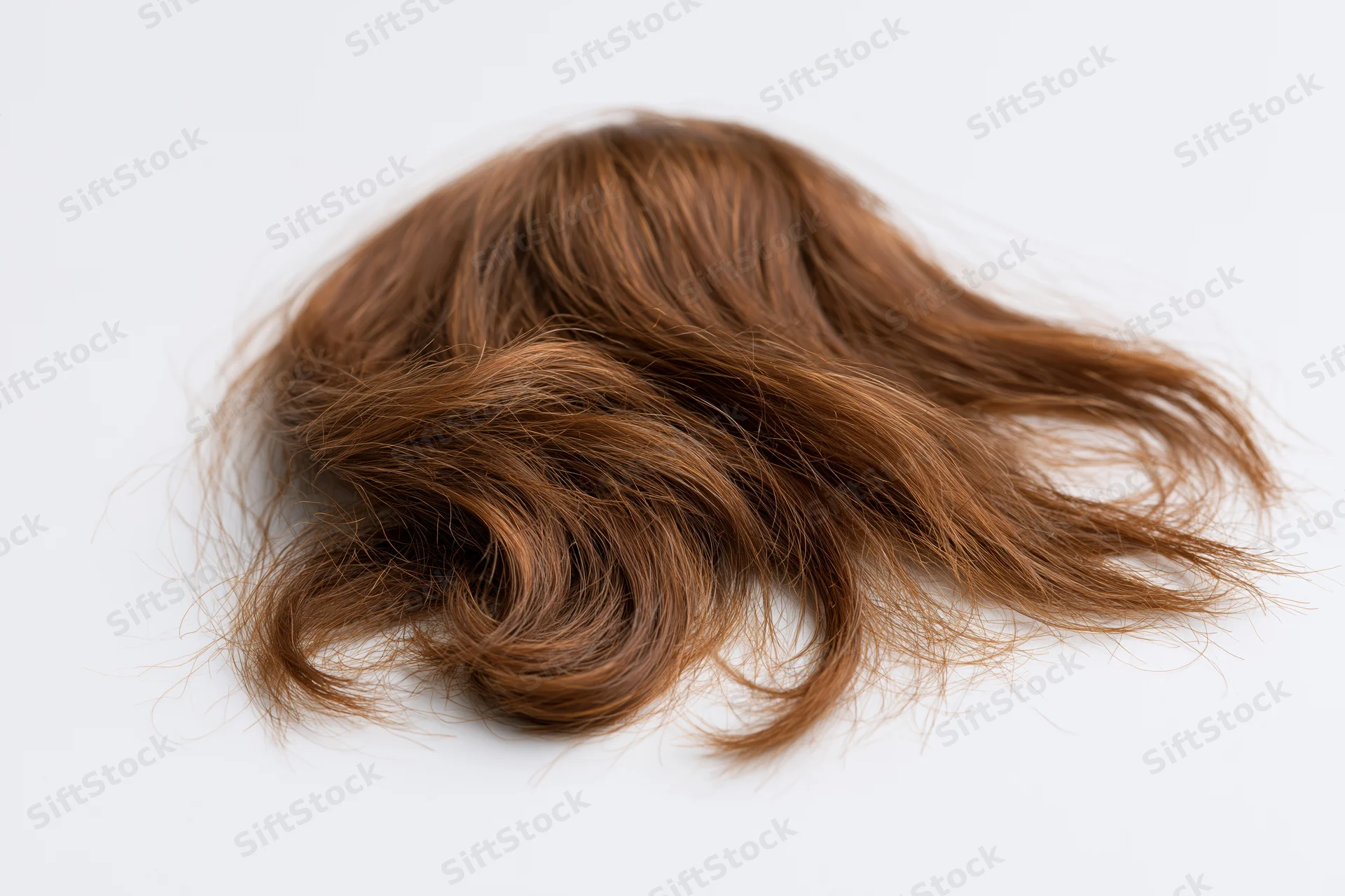 Clump of wavy brown human hair laid flat on white surface
