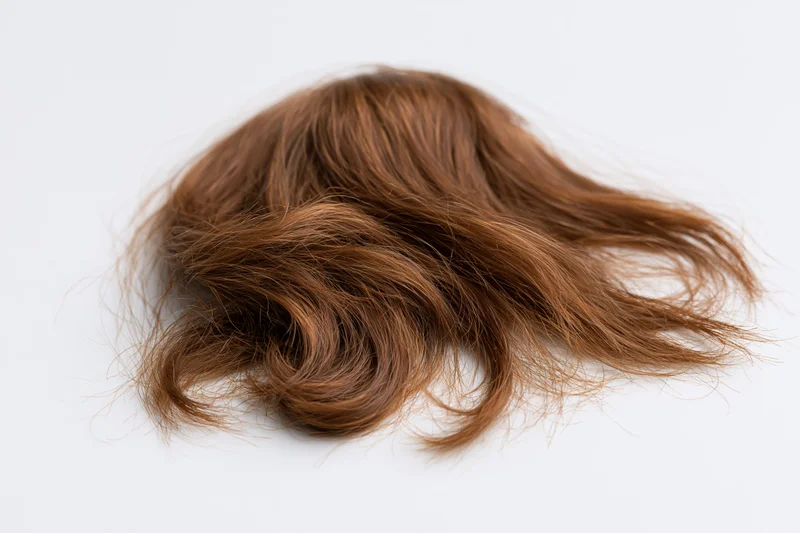 Clump of wavy brown human hair laid flat on white surface