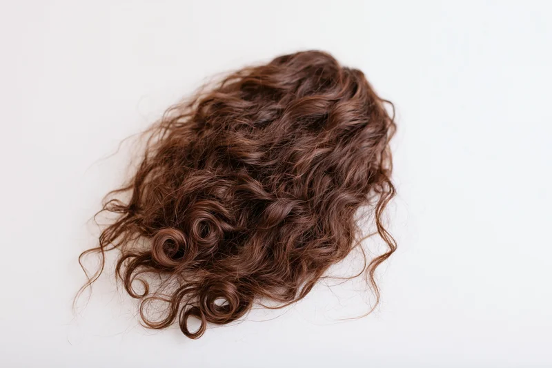 Detached clump of long curly dark brown hair lying on white surface