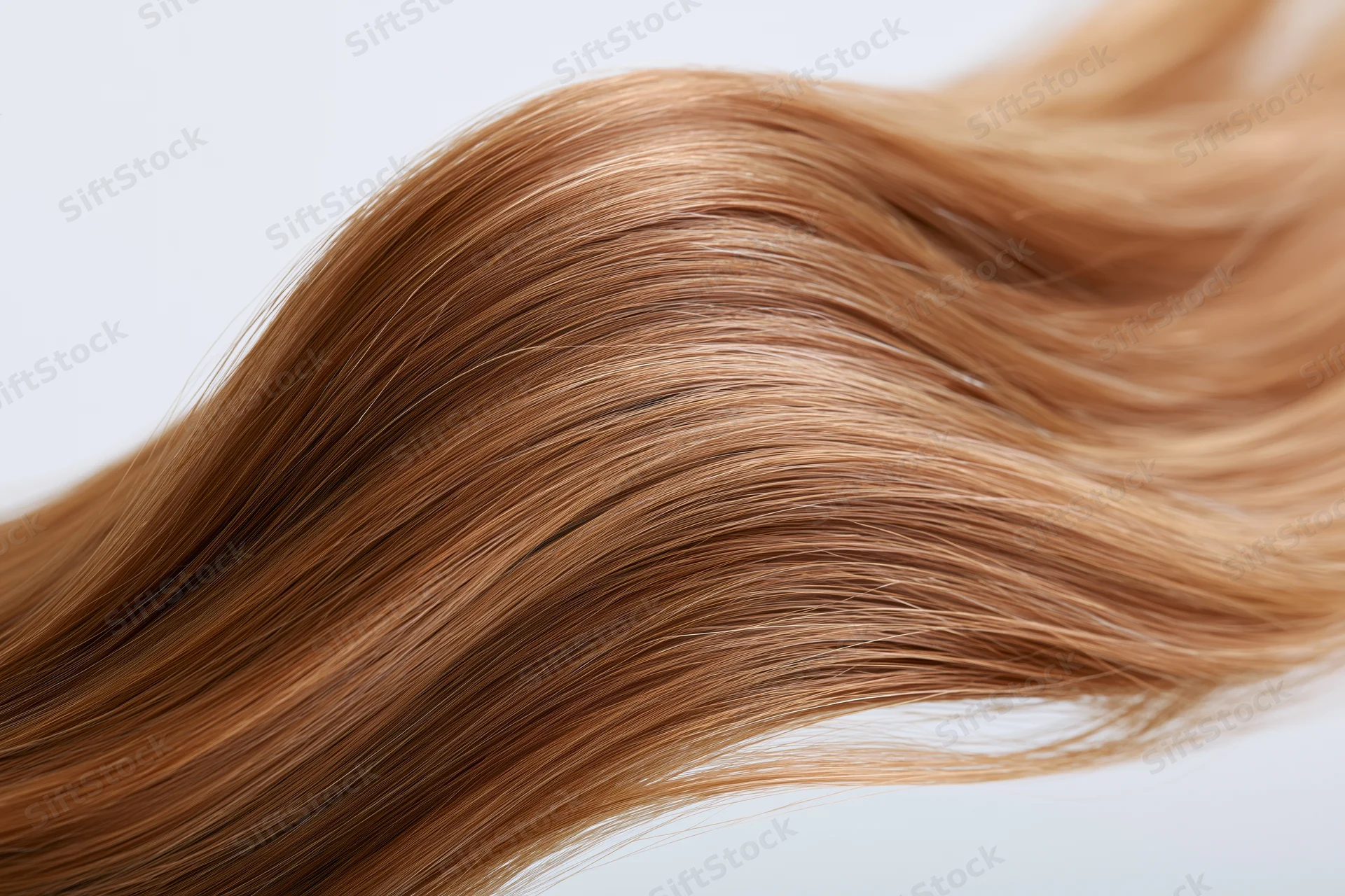 Flowing wave of straight golden-brown hair suspended midair against white background